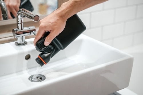 A person pouring drain cleaners into a sink