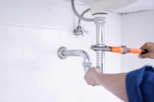 plumber uses a wrench under the sink
