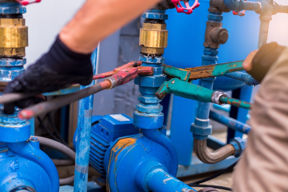 Plumber using a wrench to repair and remove the water supply pipe and valve. Plumbers working using orange pipe wrenches with blurry motor pump motor.